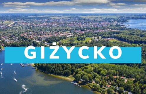 Widok na Giżycko z lotu ptaka, ukazujący jezioro, zieleń oraz zabudowę miasta otoczonego naturą. Idealne miejsce na wypoczynek i turystykę.
