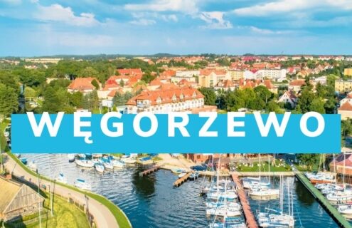Widok na Węgorzewo z lotu ptaka, ukazujący malowniczą marinę z jachtami oraz zabudowę mieszkalną otoczoną zielenią.